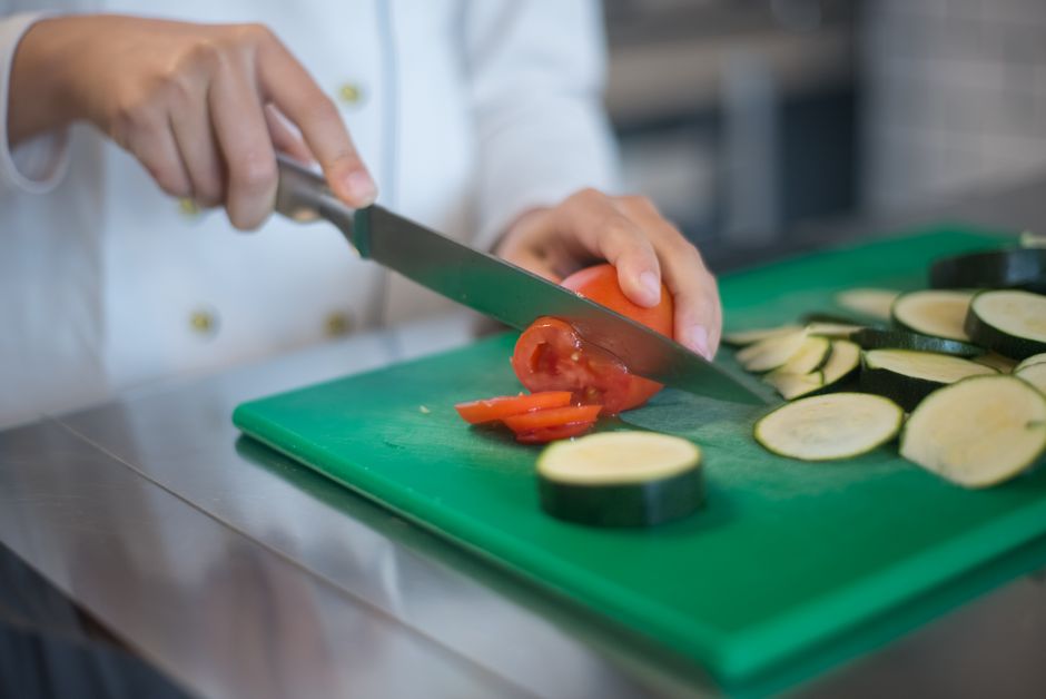 Chef precisely slices tomato and zucchini on green board, enhancing culinary presentation.