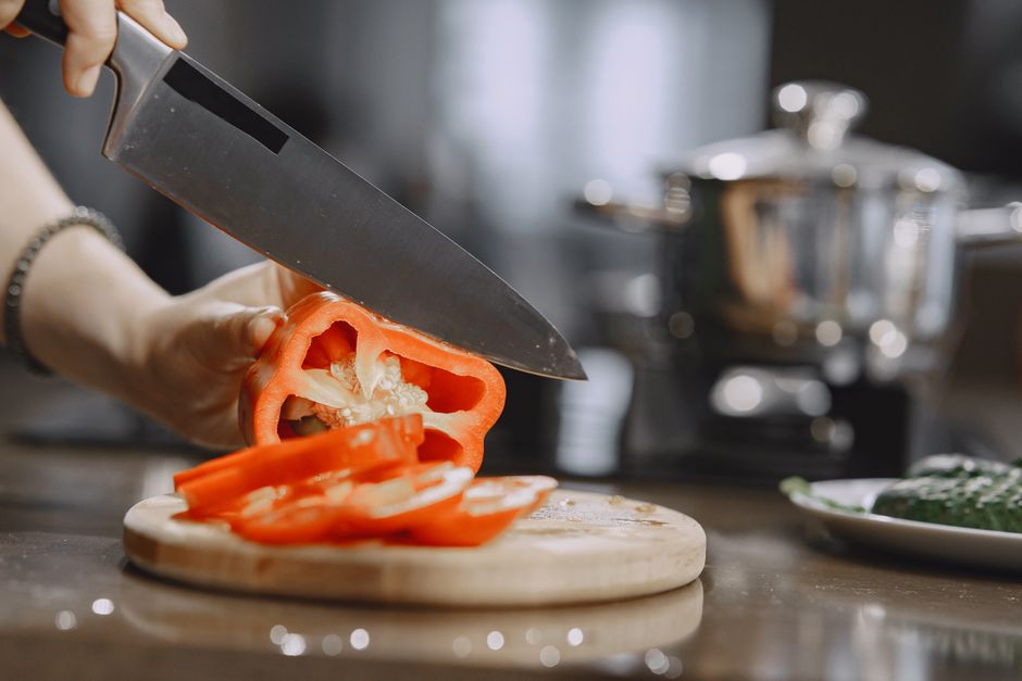 Close-up of slicing fresh red bell pepper on wooden board in modern kitchen.