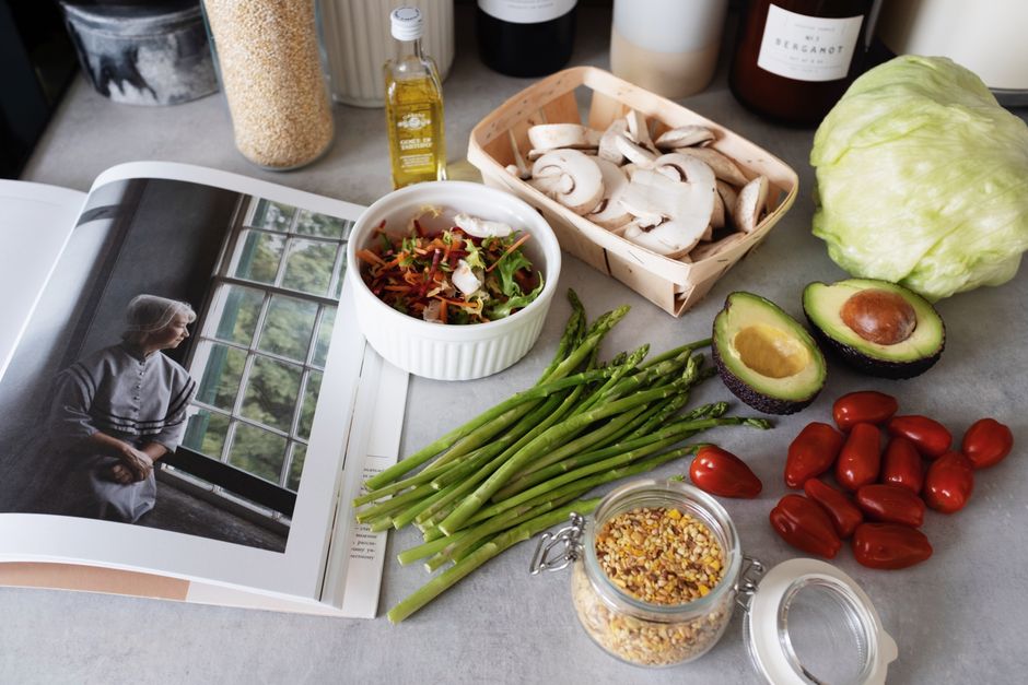 A selection of fresh vegetables and a cookbook in a kitchen setting, promoting healthy cooking.