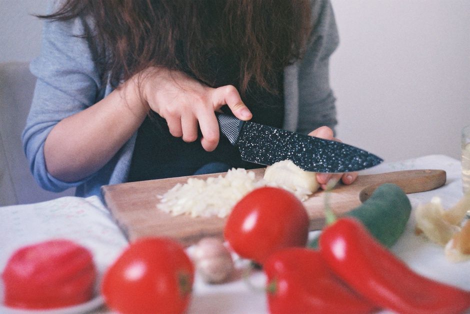 Close-up of a woman dicing onions and tomatoes on a wooden cutting board in a kitchen setting.